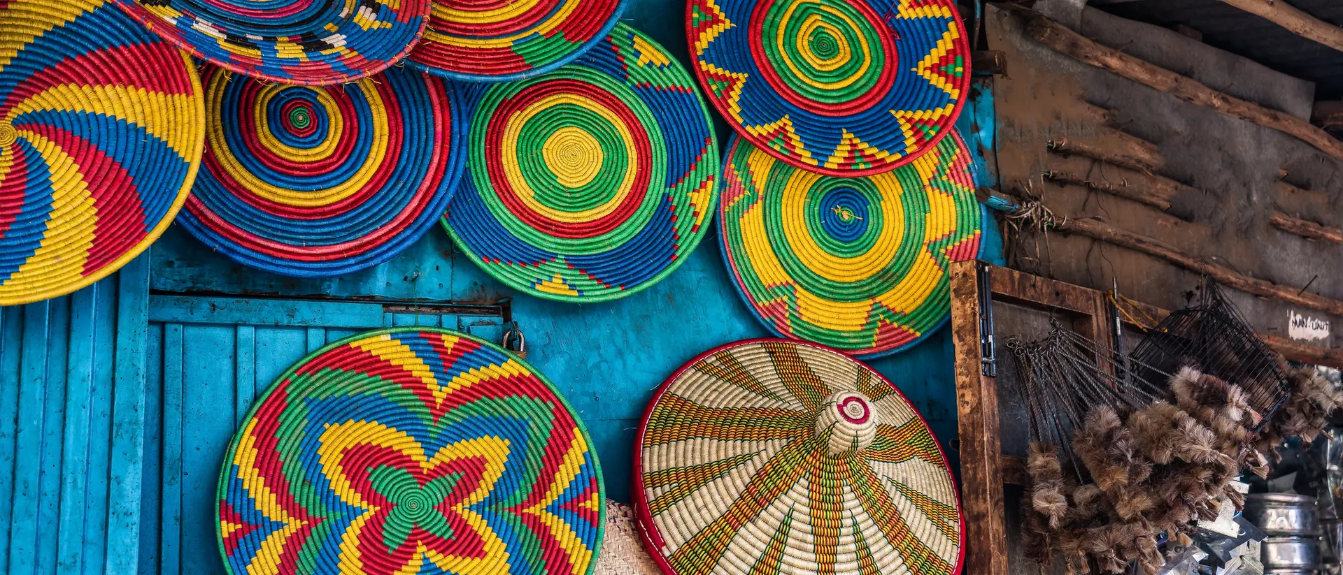 Colorful woven baskets hang against a blue wall, showcasing intricate patterns and vibrant colors in a market setting.