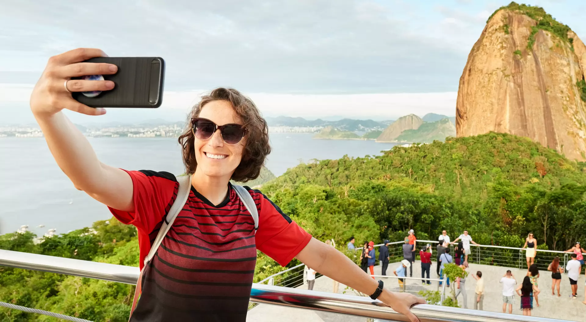 Person taking a selfie with a scenic view of a mountain and a body of water in the background.