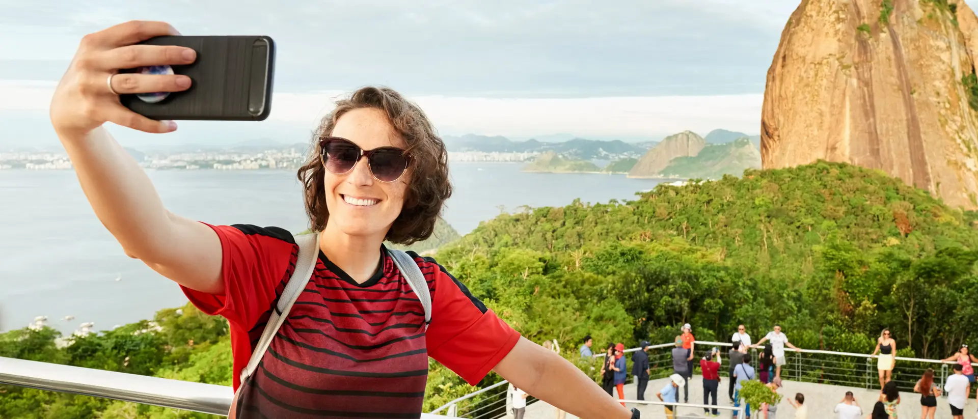 Person taking a selfie with a scenic view of a mountain and a body of water in the background.