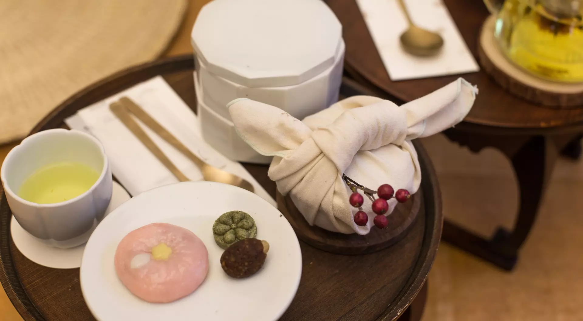 Tea and sweets displayed on a wooden table: green tea, traditional snacks, and a wrapped treat in cloth.