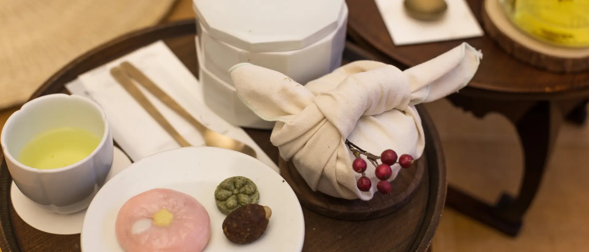 Tea and sweets displayed on a wooden table: green tea, traditional snacks, and a wrapped treat in cloth.