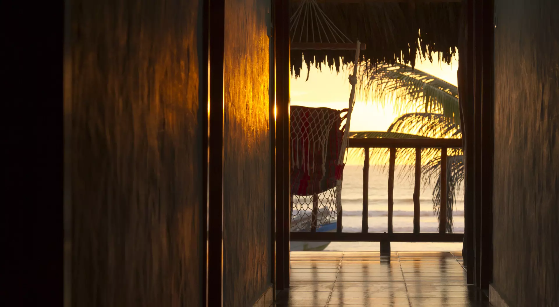 Sunset view through a hallway, showcasing a chair on a balcony with palm tree silhouettes.