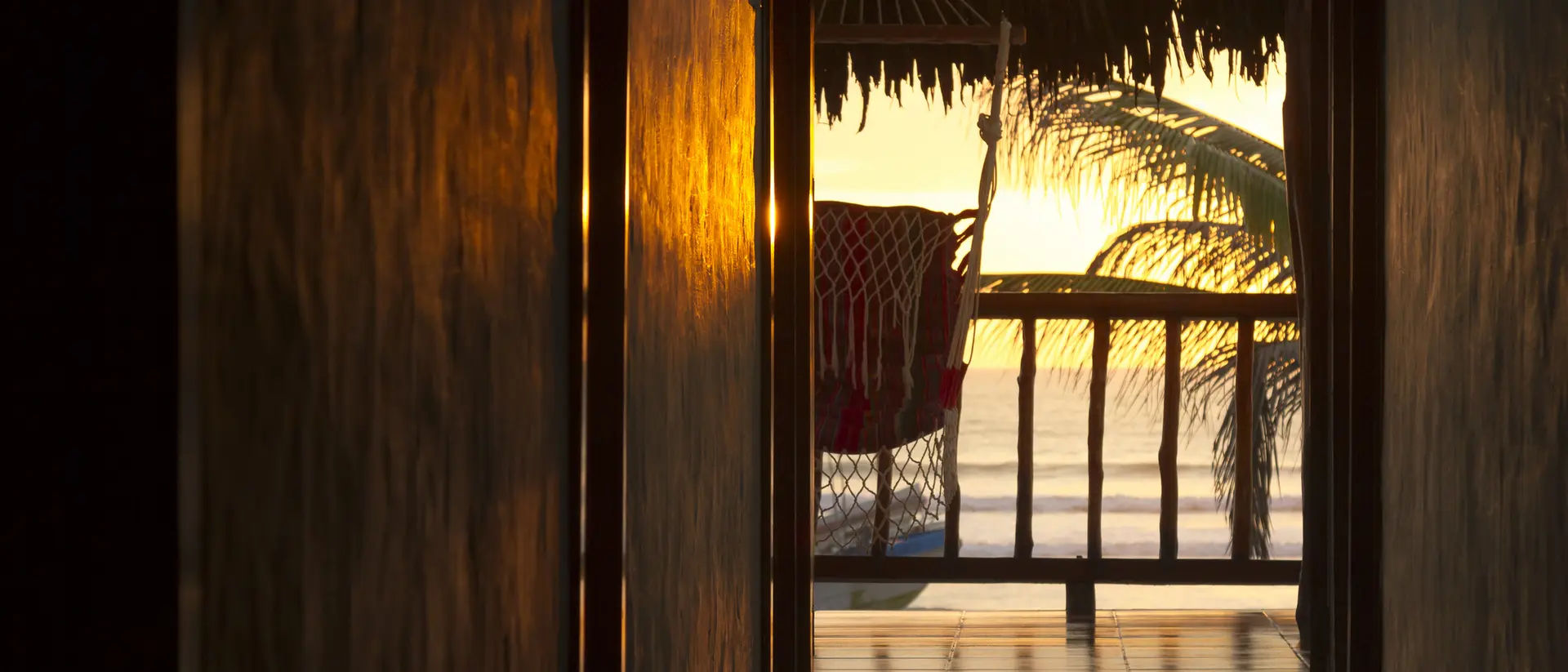 Sunset view through a hallway, showcasing a chair on a balcony with palm tree silhouettes.