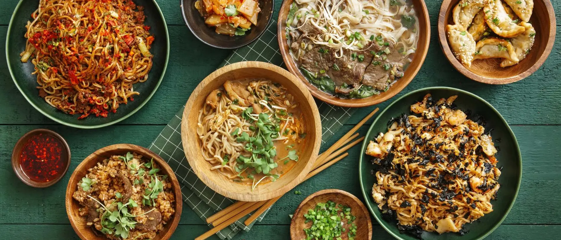 A spread of various Asian dishes including noodles, dumplings, and stir-fried vegetables on a green table.