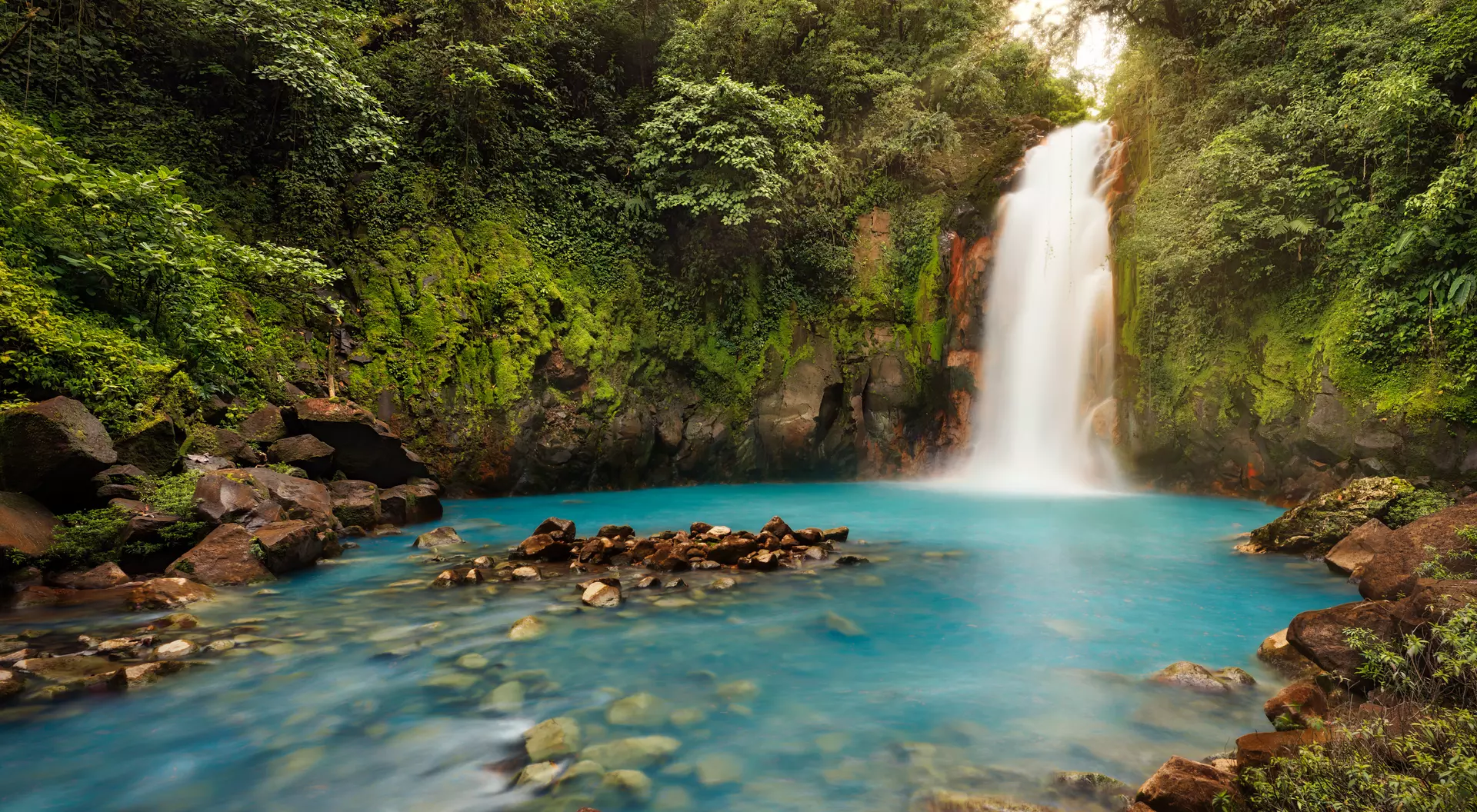 Volcán Tenorio, Alajuela The powerful Rio Celest Waterfall plunges 100 feet into a pool of bright blue water surrounded by dense tropical forest