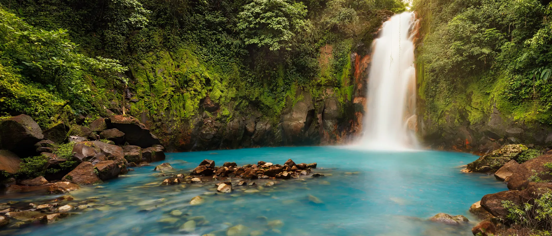 Volcán Tenorio, Alajuela The powerful Rio Celest Waterfall plunges 100 feet into a pool of bright blue water surrounded by dense tropical forest