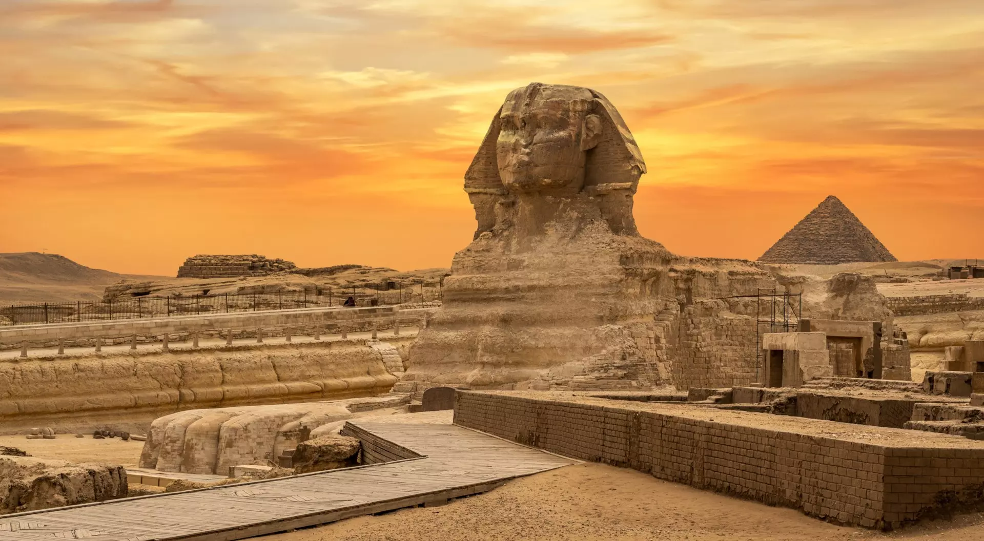 The Great Sphinx of Giza at sunset, with the Great Pyramid in the background and desert landscape surrounding.