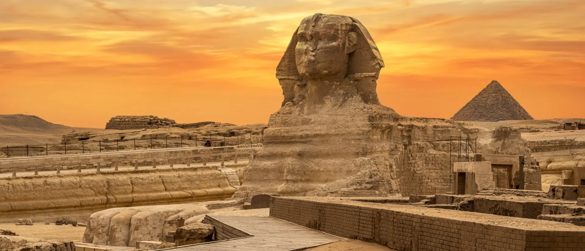 The Great Sphinx of Giza at sunset, with the Great Pyramid in the background and desert landscape surrounding.