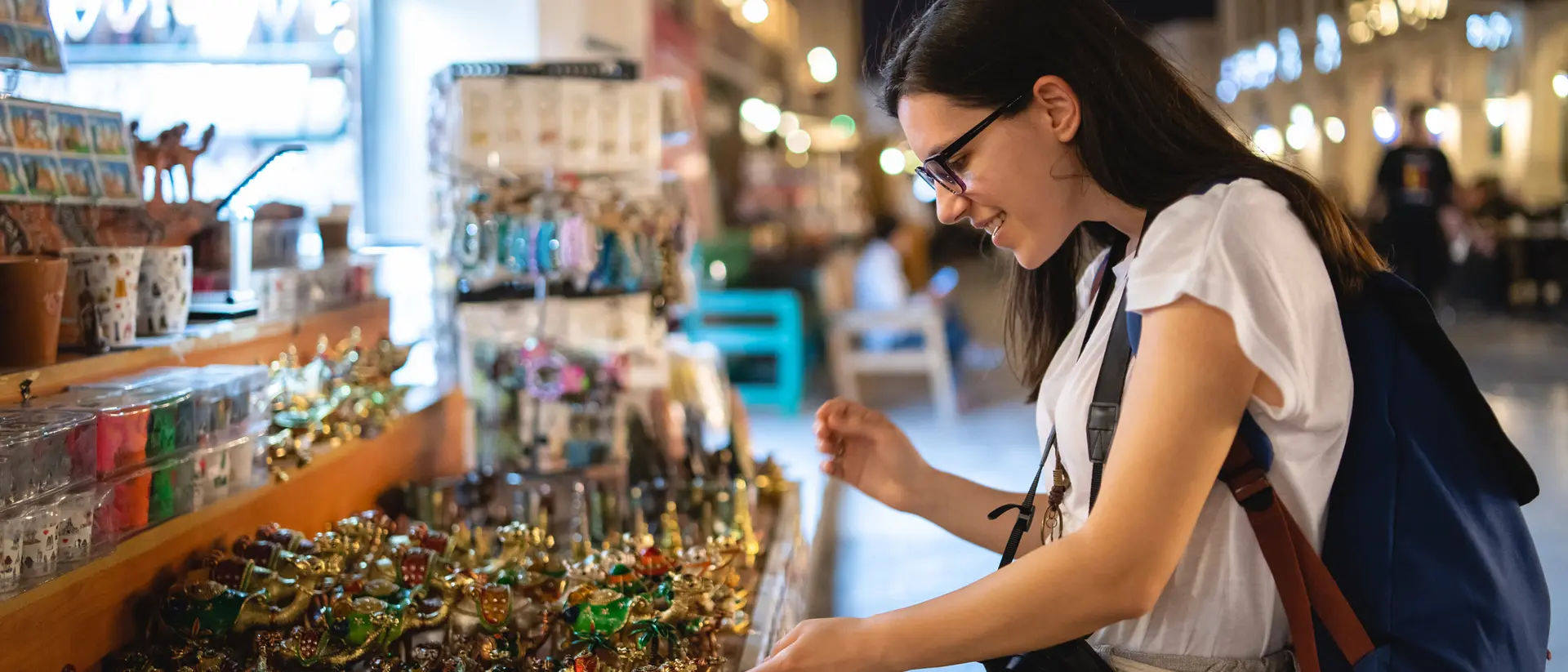 A woman smiles while browsing colorful souvenirs at a night market, surrounded by various crafts and trinkets.