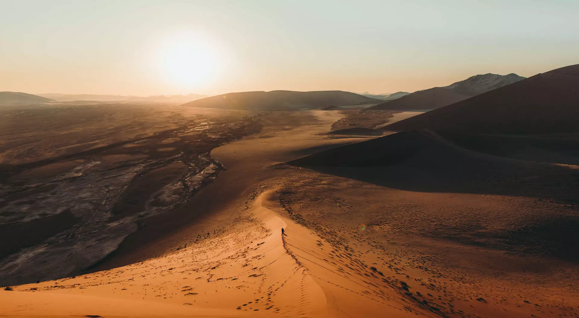 Silhouette of a man walking on the top of the big dune enjoying the dramatic bright desert sunset at Anmib-Naukluft National park
