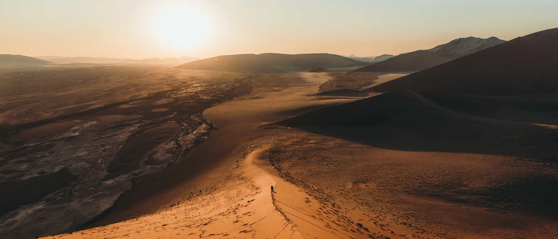 Silhouette of a man walking on the top of the big dune enjoying the dramatic bright desert sunset at Anmib-Naukluft National park
