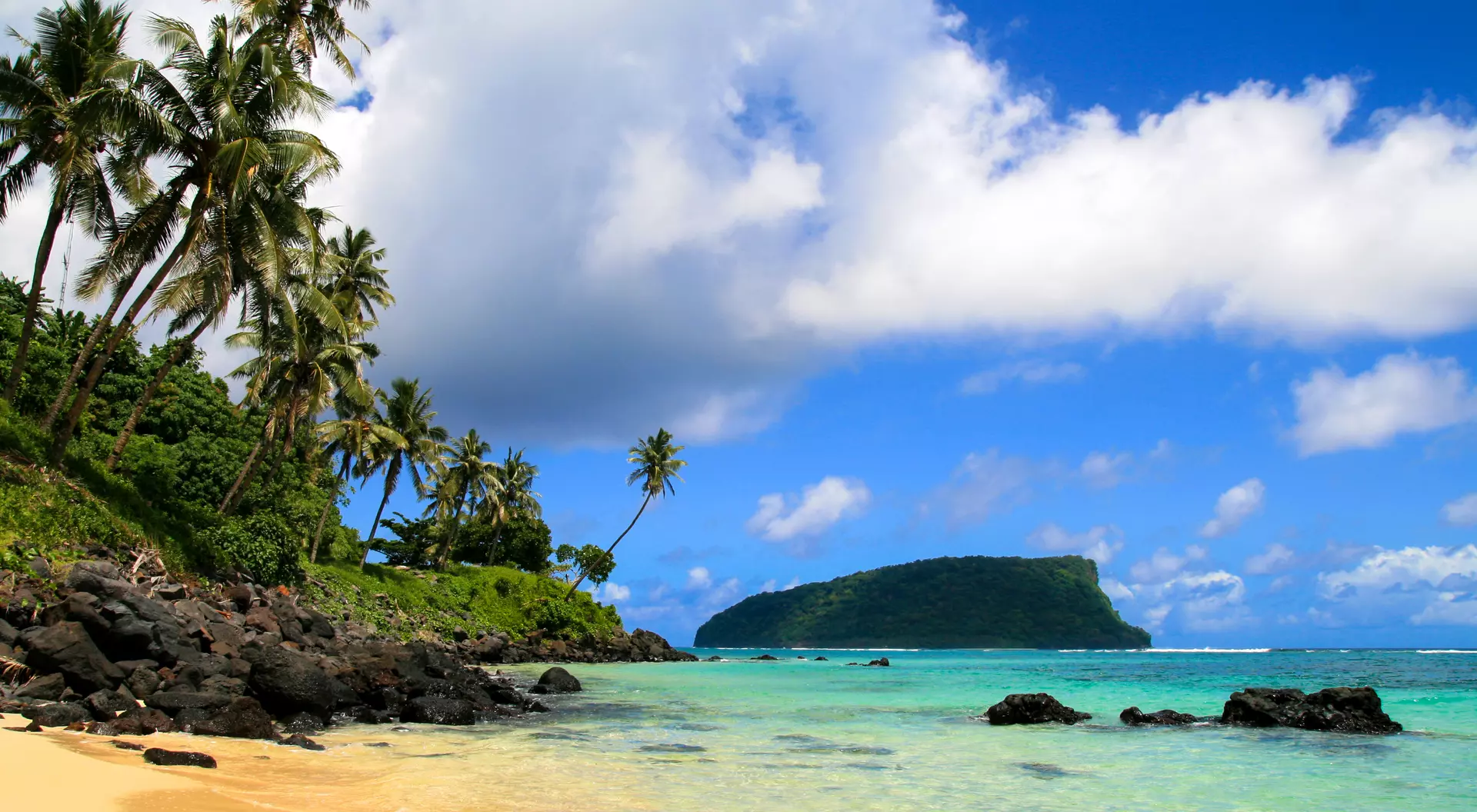 Tropical seascpape, golden sandy beach with palm trees and pristine blue waters of Pacific Ocean, view from Upolu to Nu'utele Island