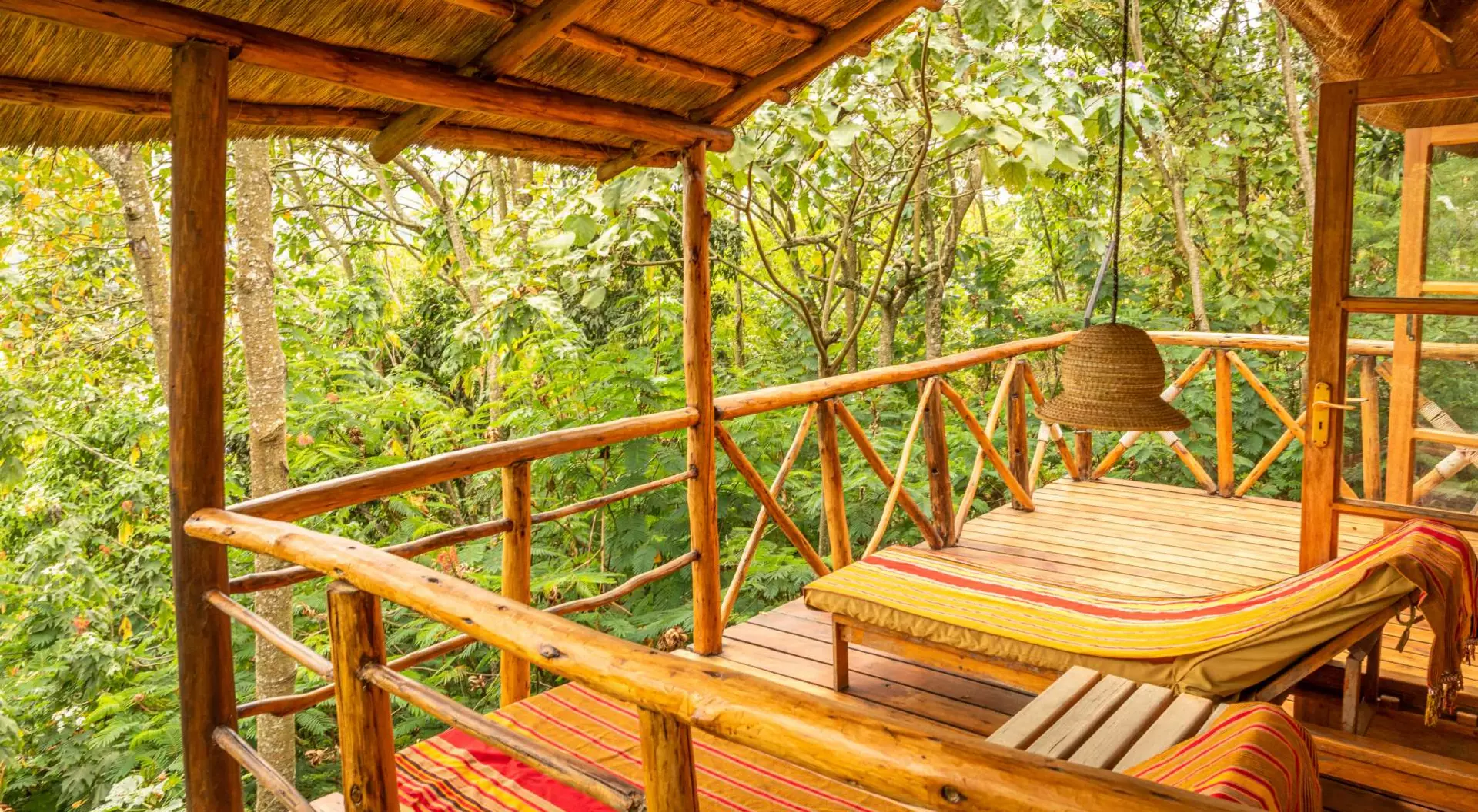 Cozy wooden balcony with striped loungers, surrounded by lush greenery and a hanging light fixture.
