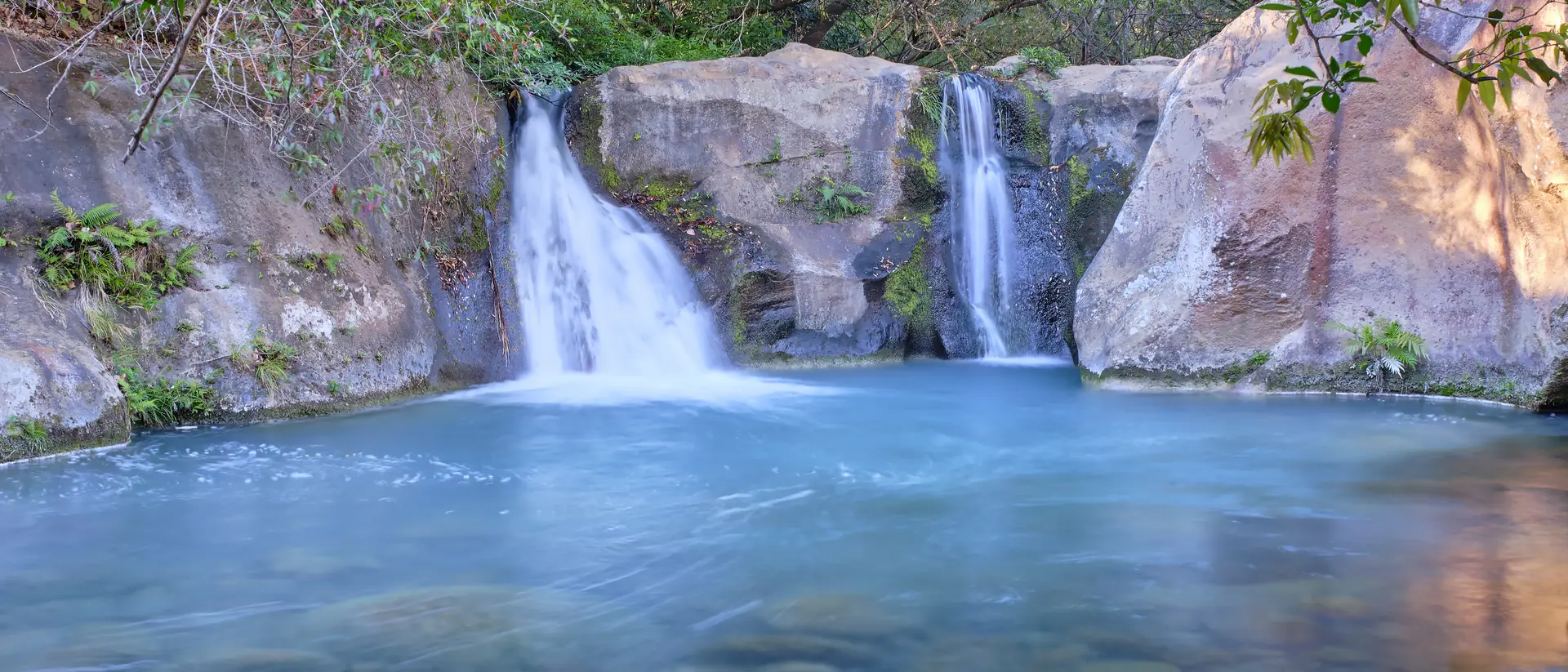 Beautiful blue logoon are surrounded by volcanic rock walls and green foliage