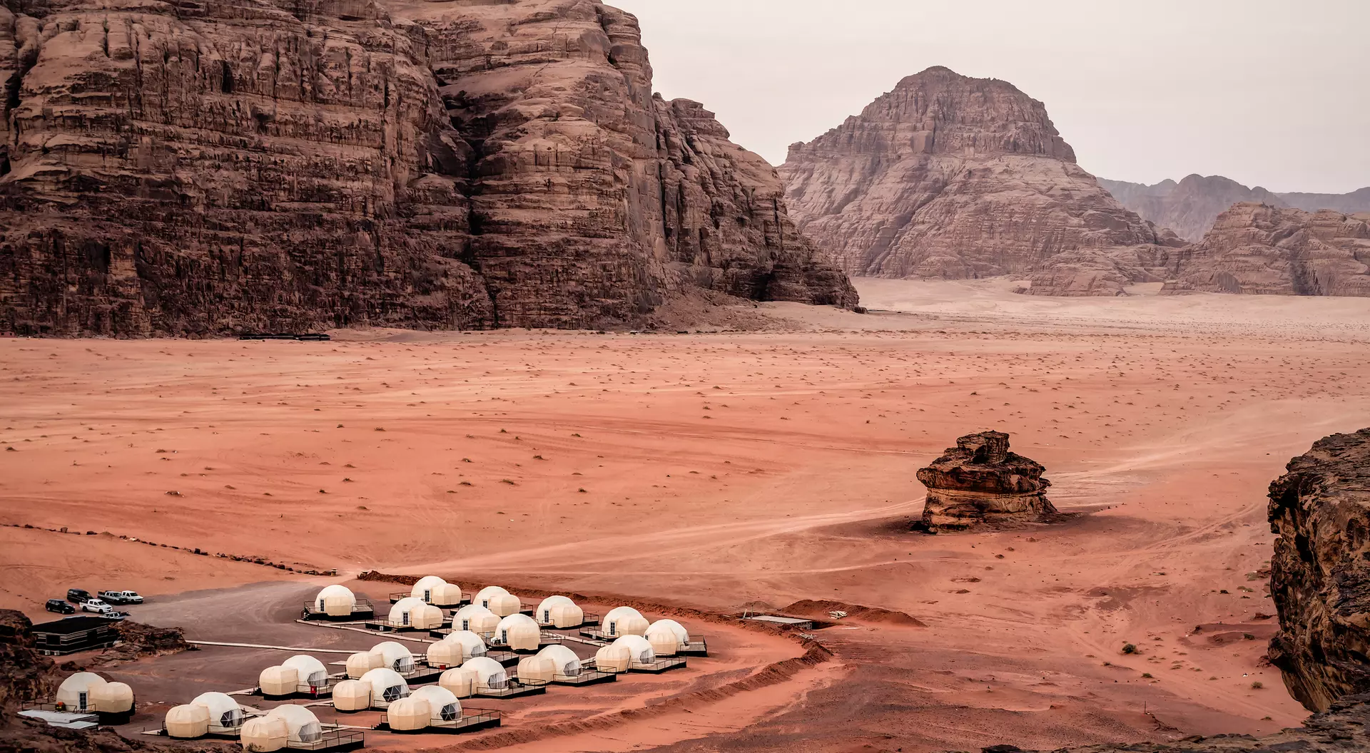 White dome tents in a sandy desert landscape surrounded by rocky mountains at dusk.