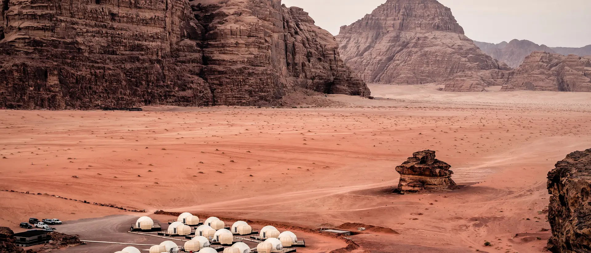 White dome tents in a sandy desert landscape surrounded by rocky mountains at dusk.