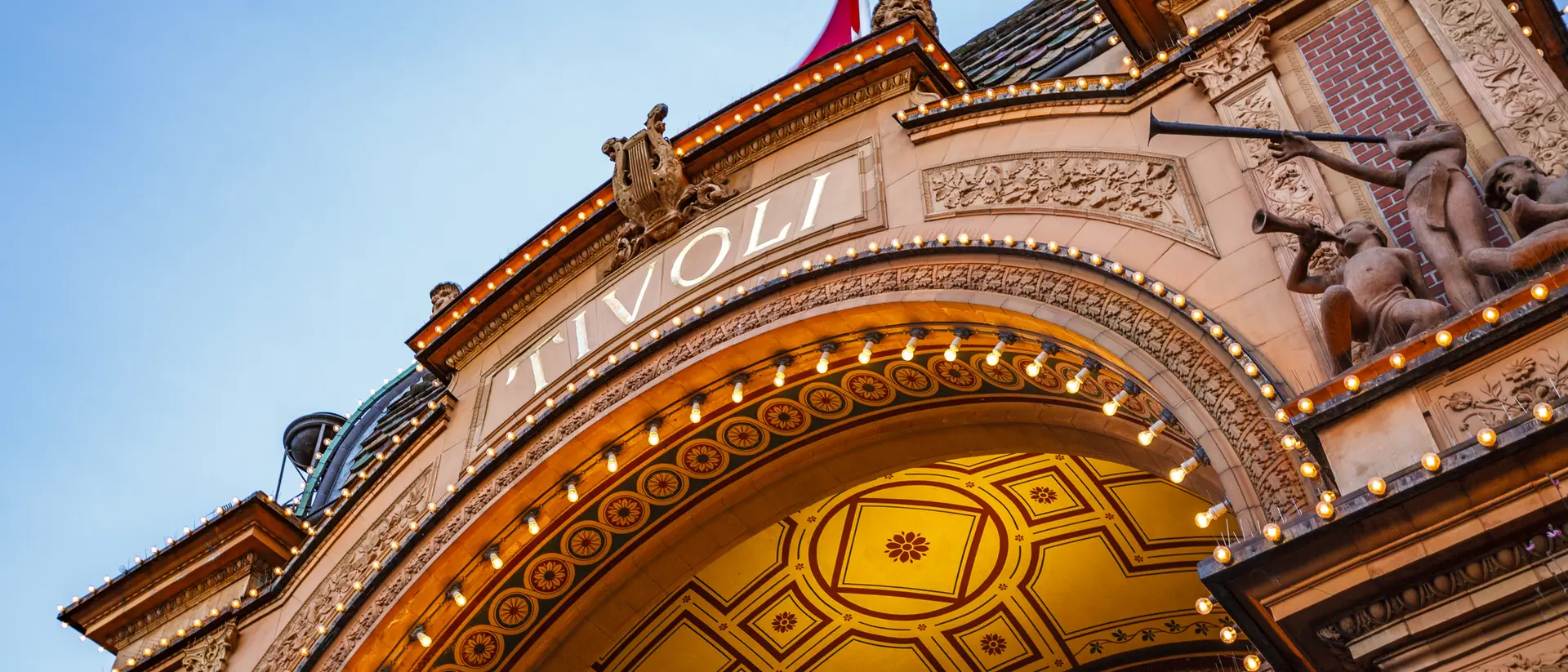 Archway of Tivoli Gardens, adorned with lights and decorative sculptures, against a clear sky.