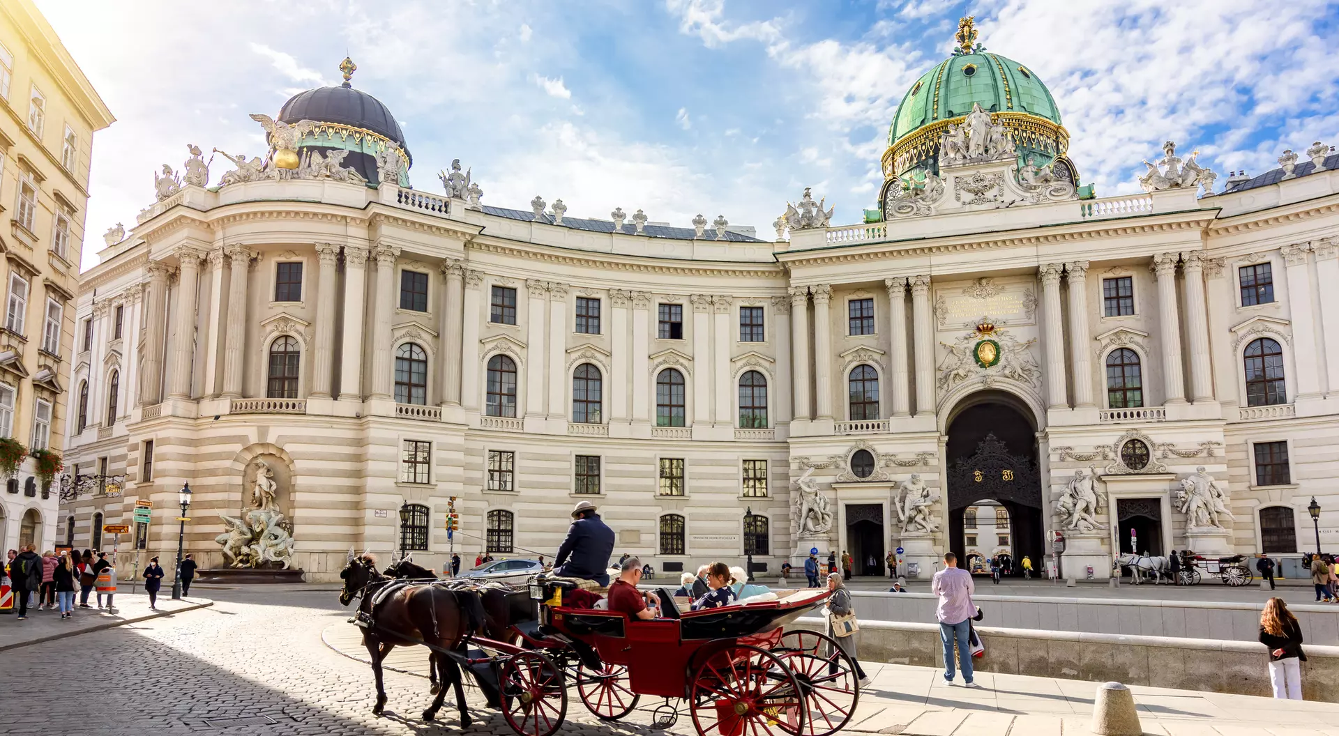 Horse-drawn carriage in front of a grand, historic building with a green dome under a blue sky.