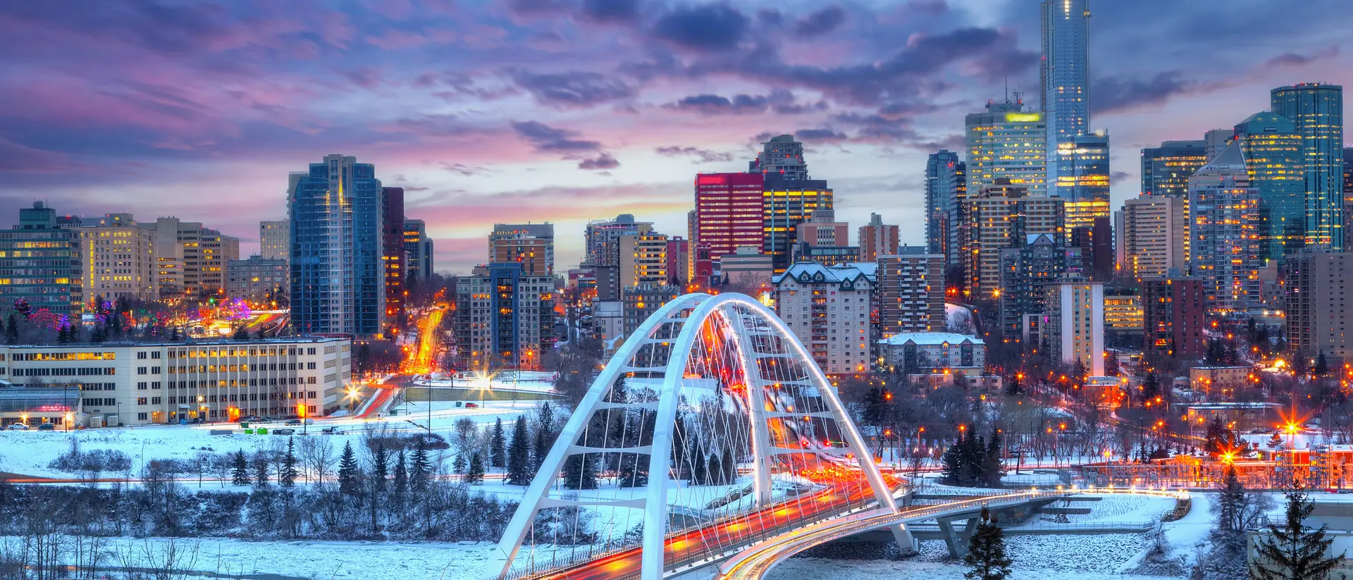 Edmonton, Canada Light trails from rush hour traffic light up downtown Winter sunset skyline showing Walterdale Bridge across the frozen, snow-covered Saskatchewan River and surrounding skyscrapers.