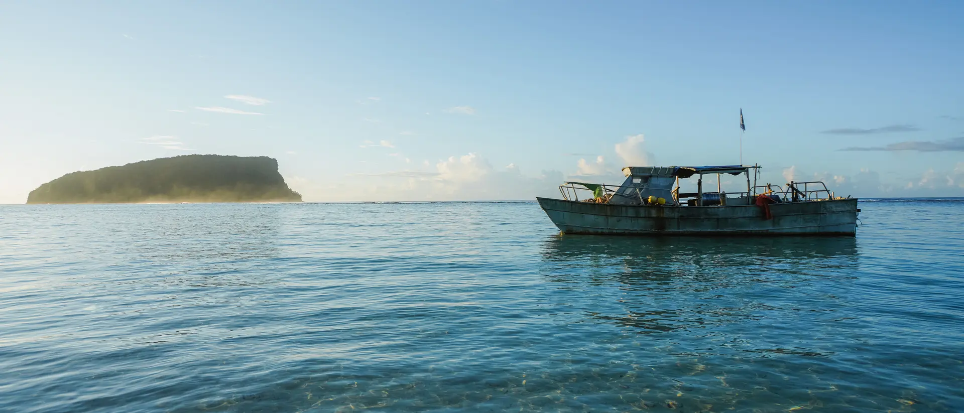 A small boat floats in clear water, with a distant island visible under a bright blue sky.