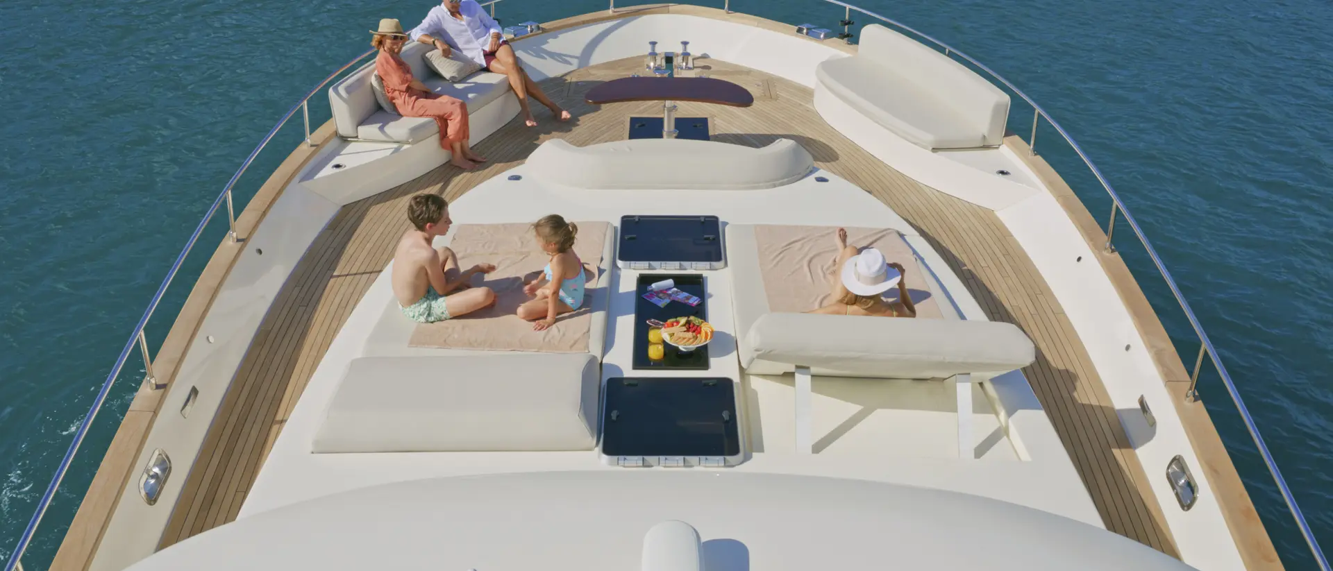 People relax on a yacht's deck, enjoying the sun and ocean view, with seating and refreshments nearby.