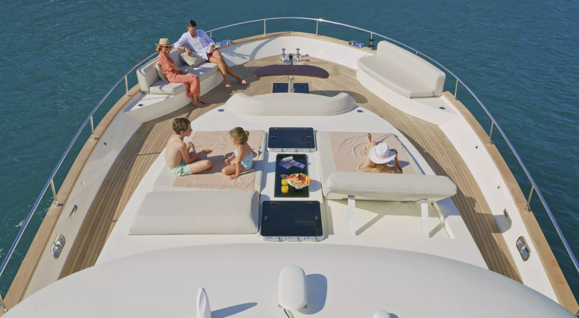 People relax on a yacht's deck, enjoying the sun and ocean view, with seating and refreshments nearby.