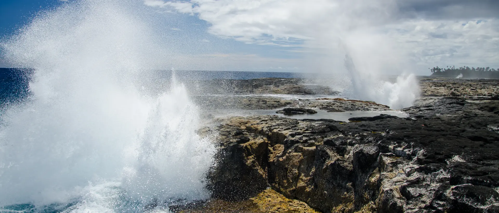 The Alofaaga Blowholes send water towards the bright blue sky along the ocean in Somoa