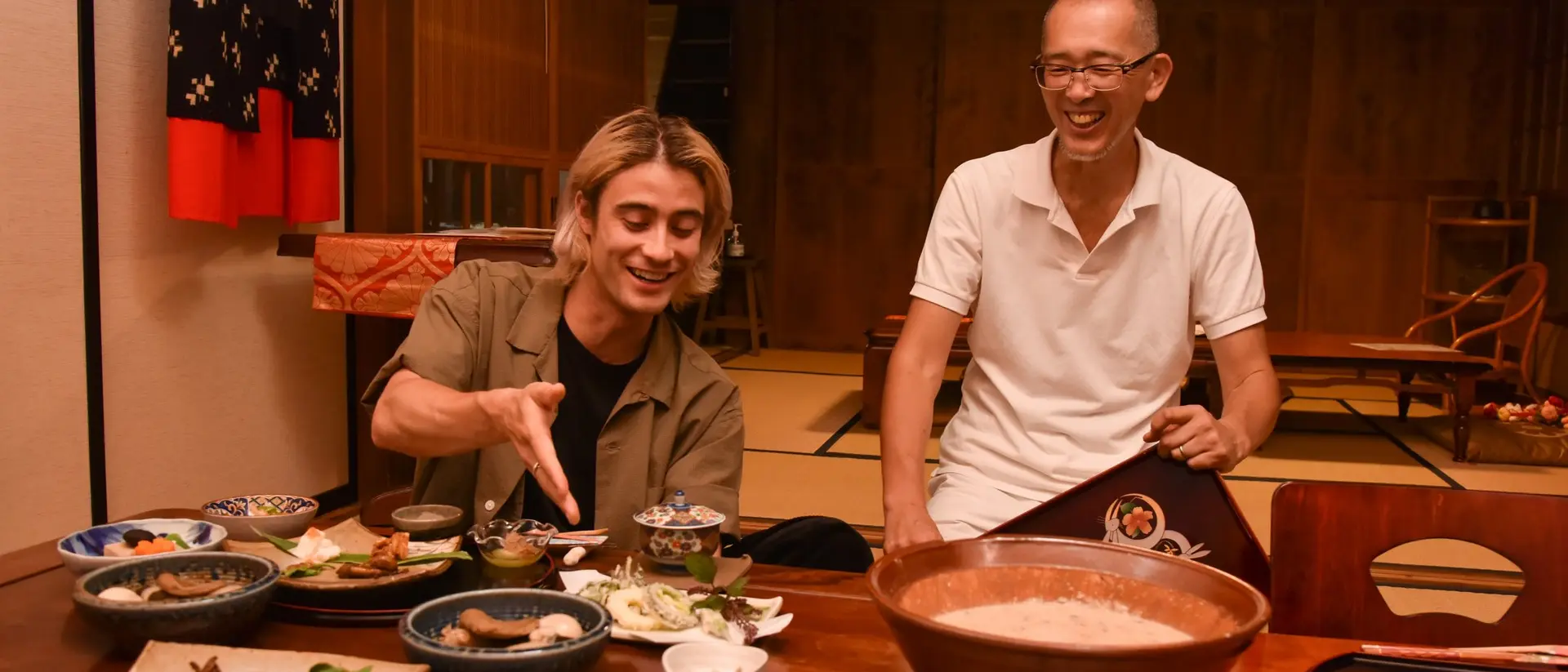 Two men enjoying a meal at a traditional Japanese table, surrounded by various dishes and smiling at each other.