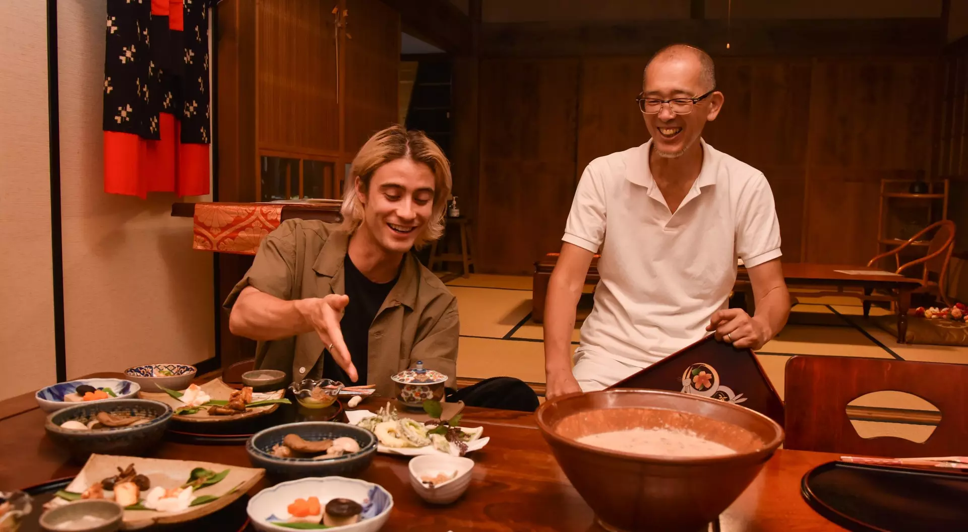 Two men enjoying a meal at a traditional Japanese table, surrounded by various dishes and smiling at each other.