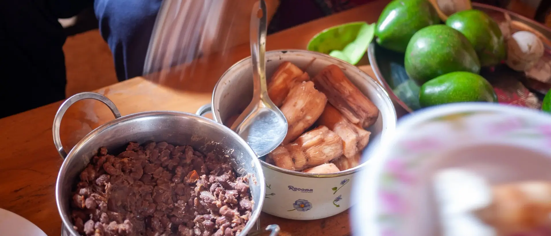 A table with bowls of ground meat and fried plantains, surrounded by fresh avocados and plates of food.