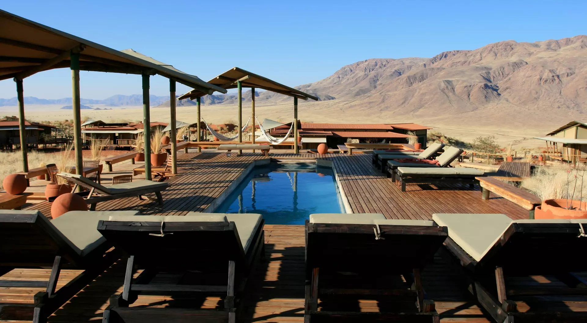 A serene outdoor pool area with lounge chairs, surrounded by mountain views and desert landscape under a clear blue sky.
