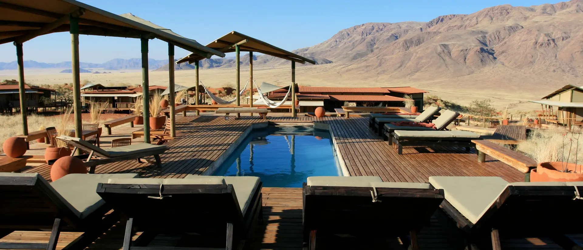 A serene outdoor pool area with lounge chairs, surrounded by mountain views and desert landscape under a clear blue sky.
