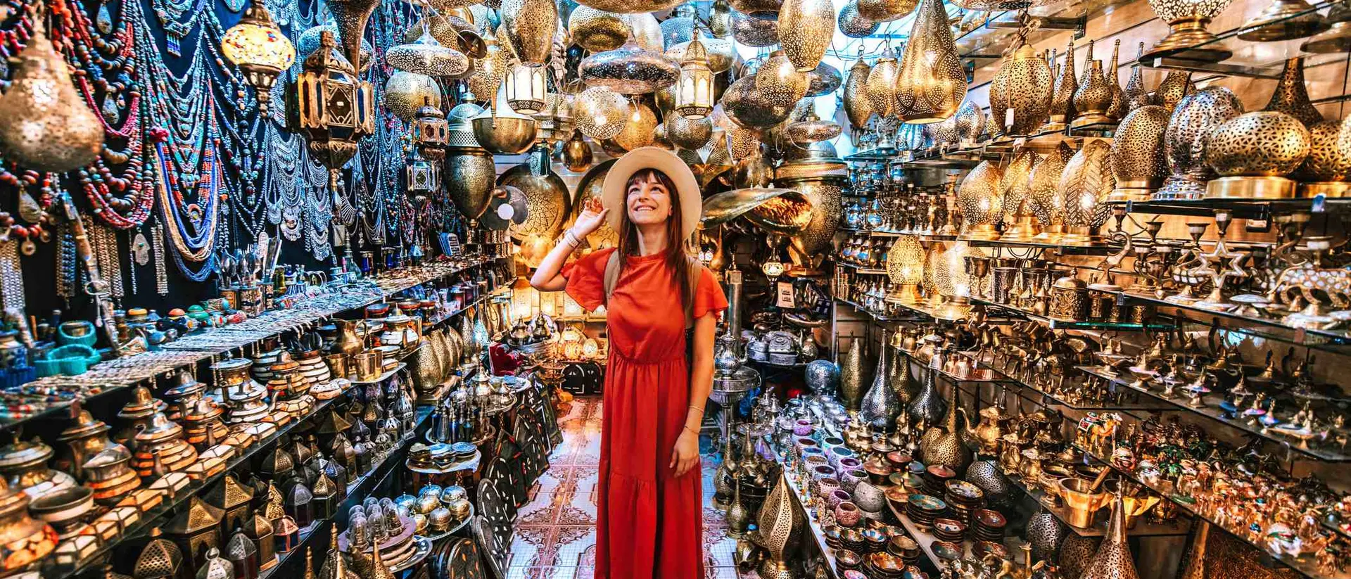 Person in a red dress and hat stands in a vibrant shop filled with intricate metal lanterns and decorative items.