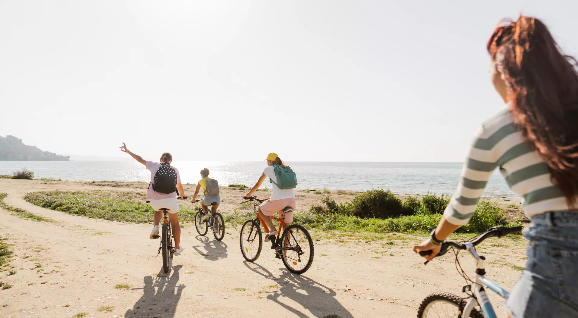Four people ride bicycles along a beach path, enjoying a sunny day by the ocean.