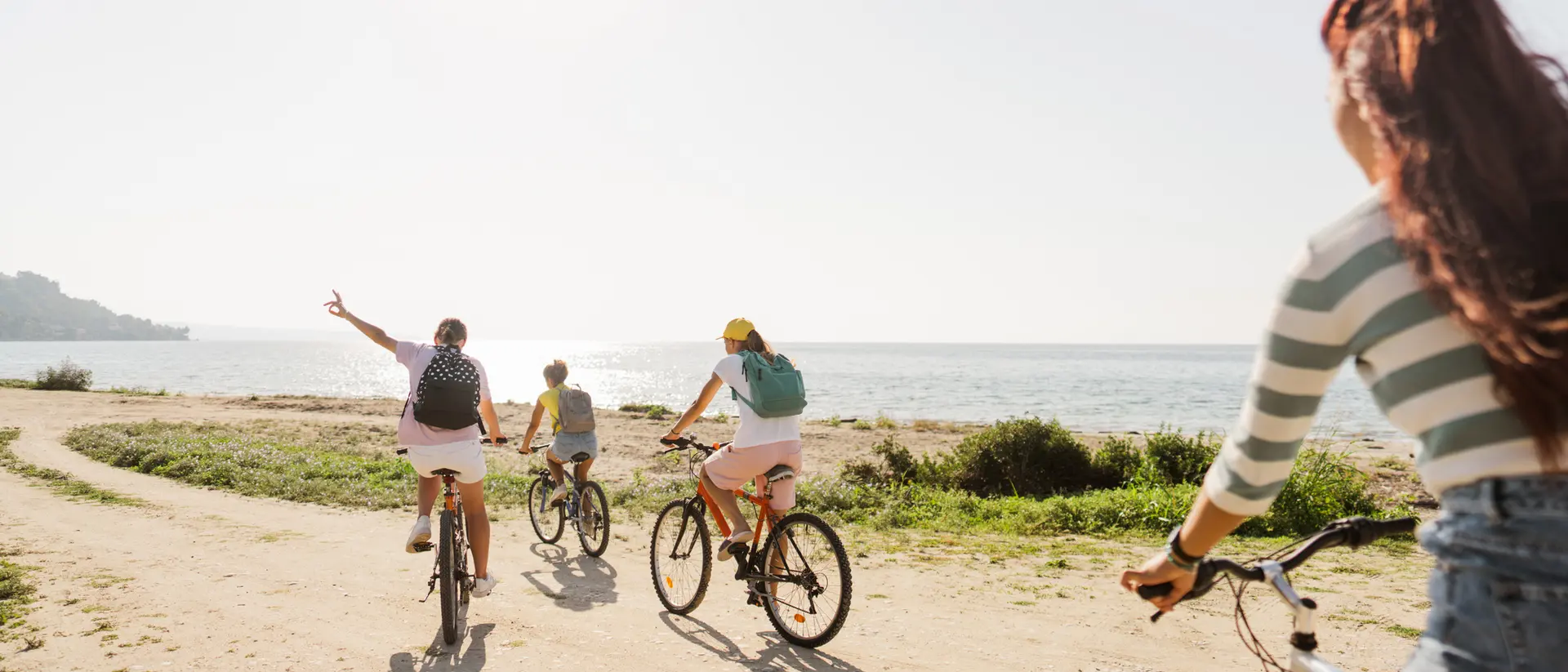 Four people ride bicycles along a beach path, enjoying a sunny day by the ocean.