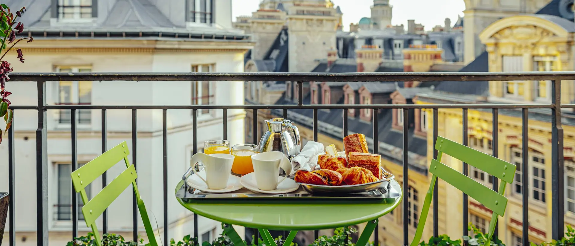 A green table with breakfast items overlooks a cityscape, featuring buildings and a dome in the background.