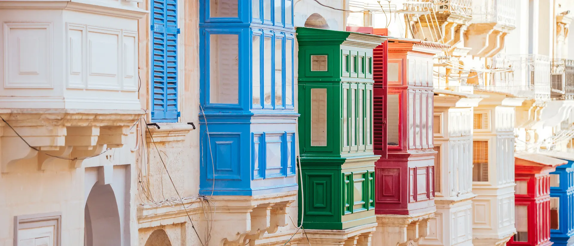 Colorful balconies in blue, green, red, and white line a narrow street, showcasing vibrant architectural details.