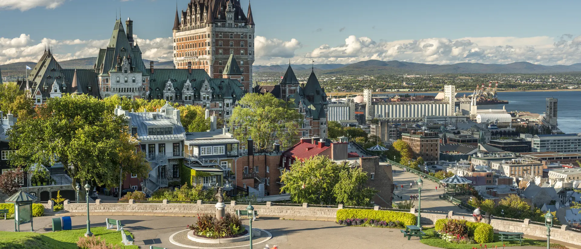 A scenic view of Quebec City featuring the iconic Chateau Frontenac, surrounded by green spaces and colorful flowers.