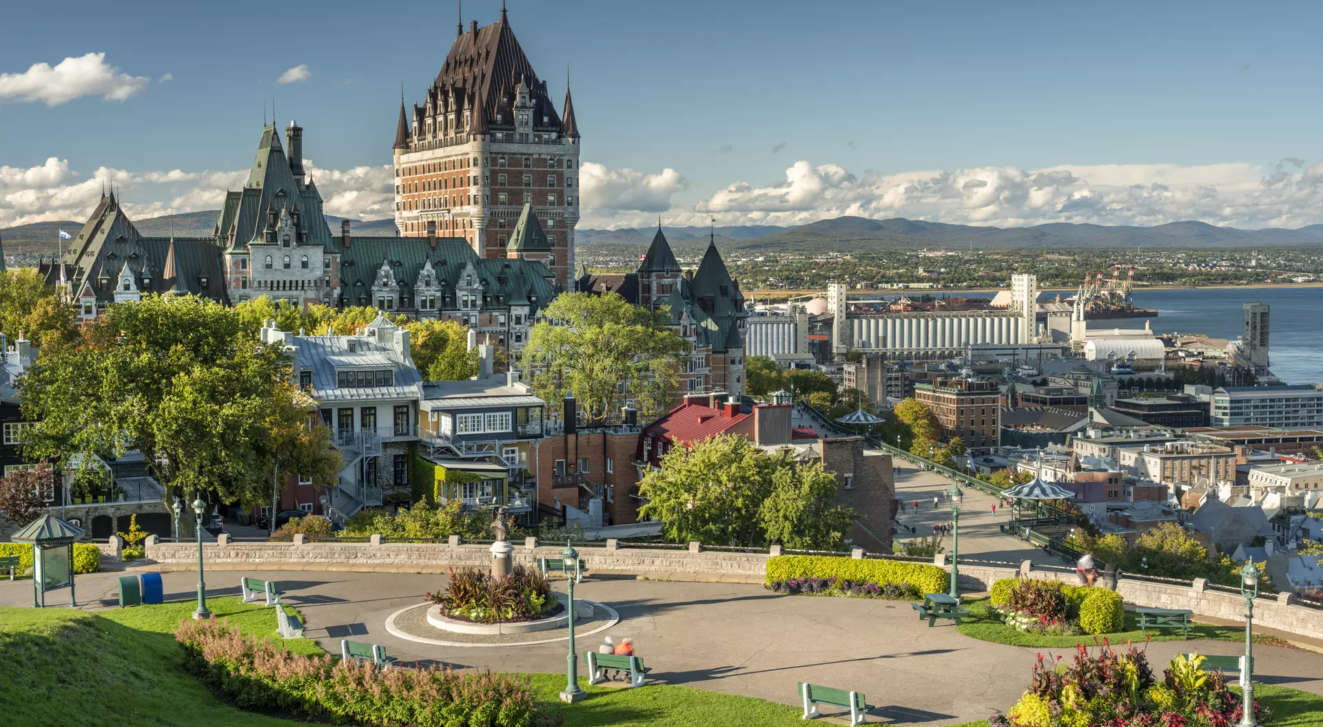 A scenic view of Quebec City featuring the iconic Chateau Frontenac, surrounded by green spaces and colorful flowers.