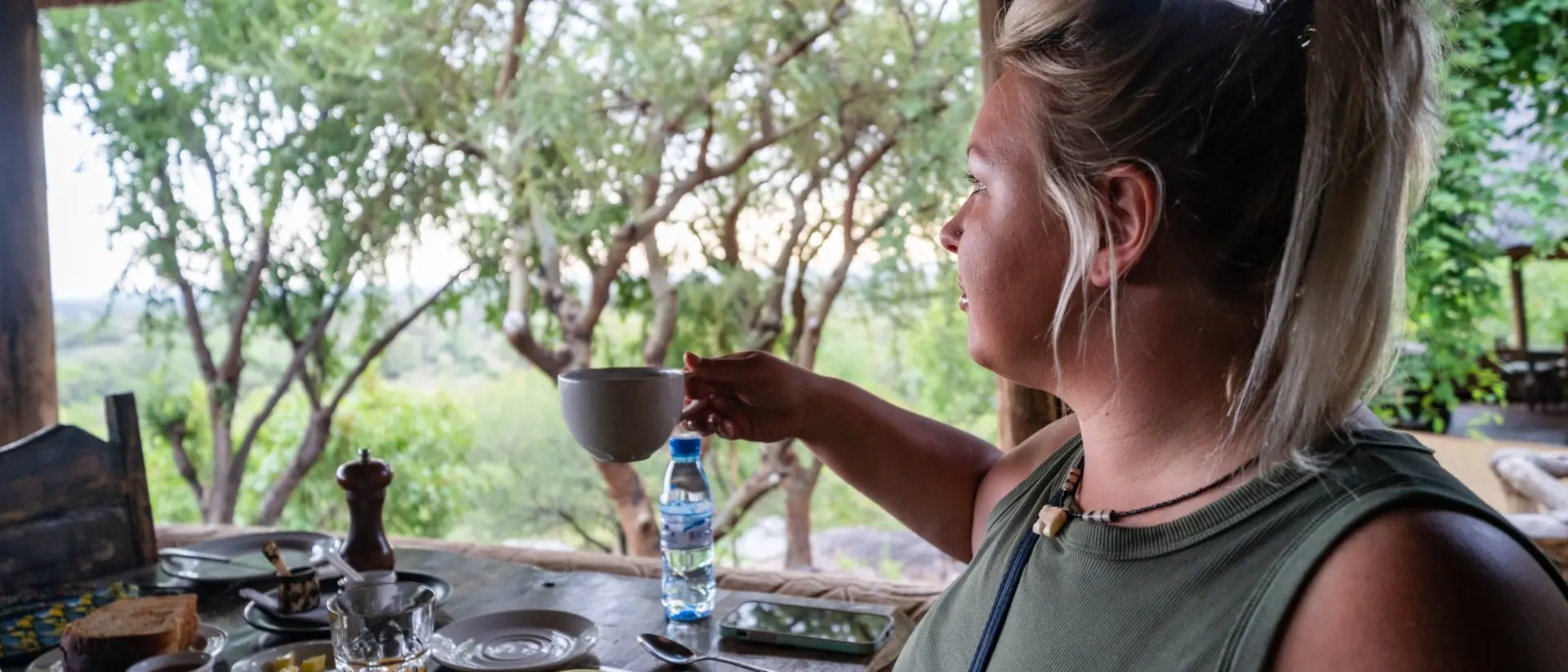 A person enjoying breakfast with fruits and drinks at an outdoor table, overlooking a scenic green landscape.