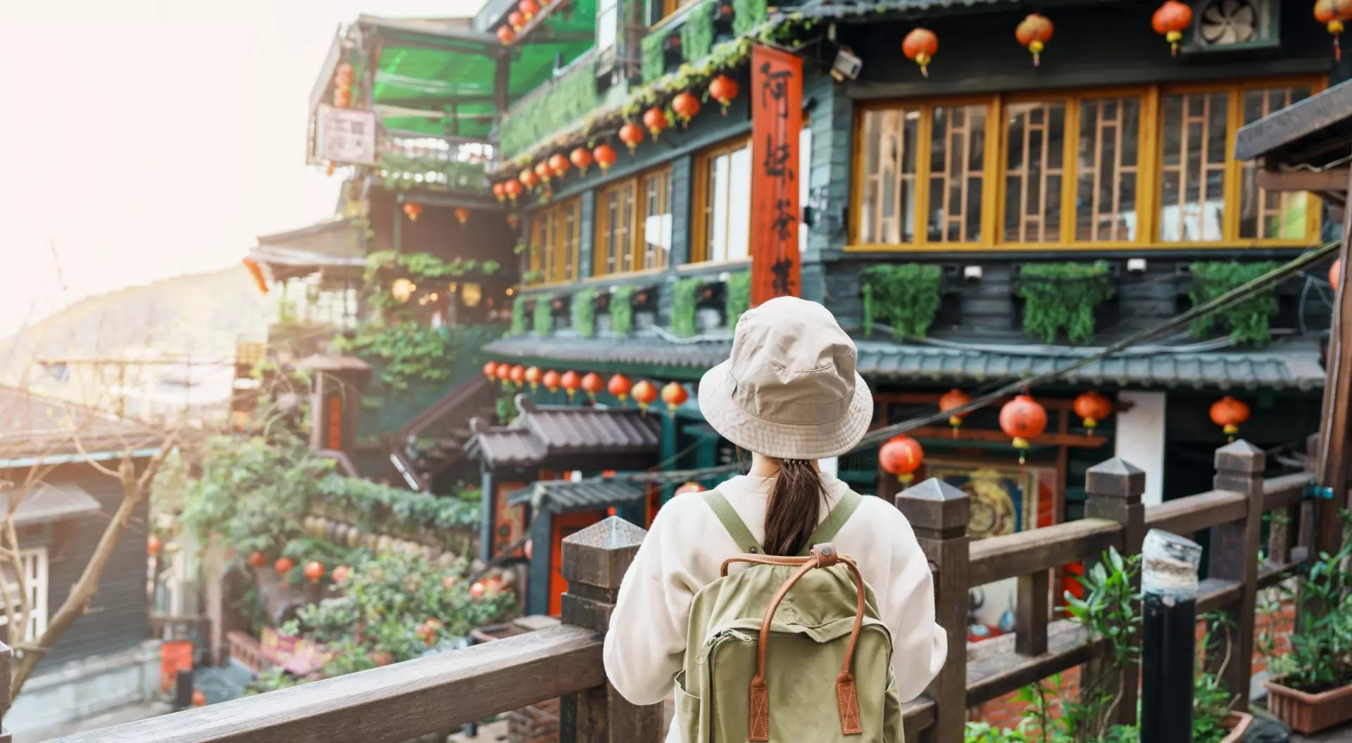 Person in a hat and backpack gazes at a colorful, traditional building adorned with lanterns and greenery.