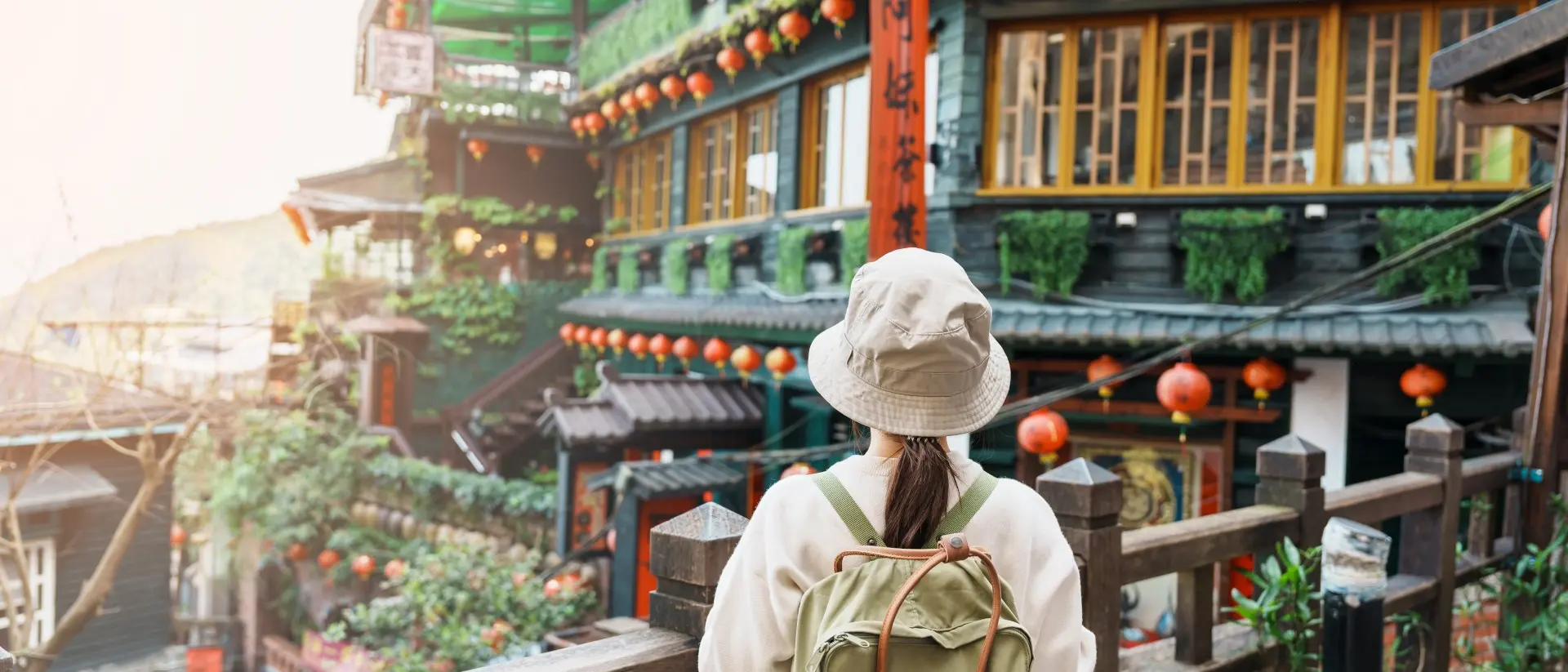 Person in a hat and backpack gazes at a colorful, traditional building adorned with lanterns and greenery.