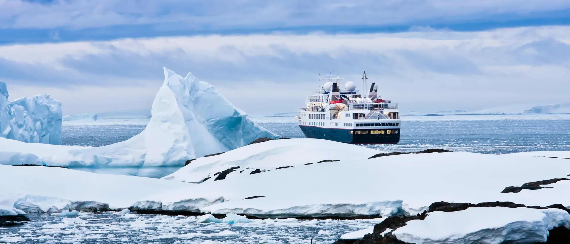 A cruise ship navigates icy waters near large glaciers and floating ice in a serene Arctic landscape.