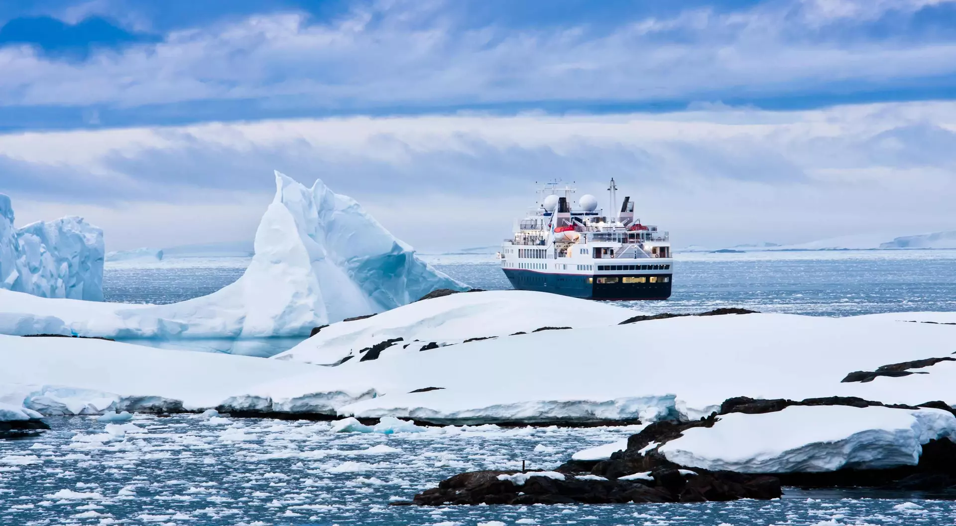 A cruise ship navigates icy waters near large glaciers and floating ice in a serene Arctic landscape.
