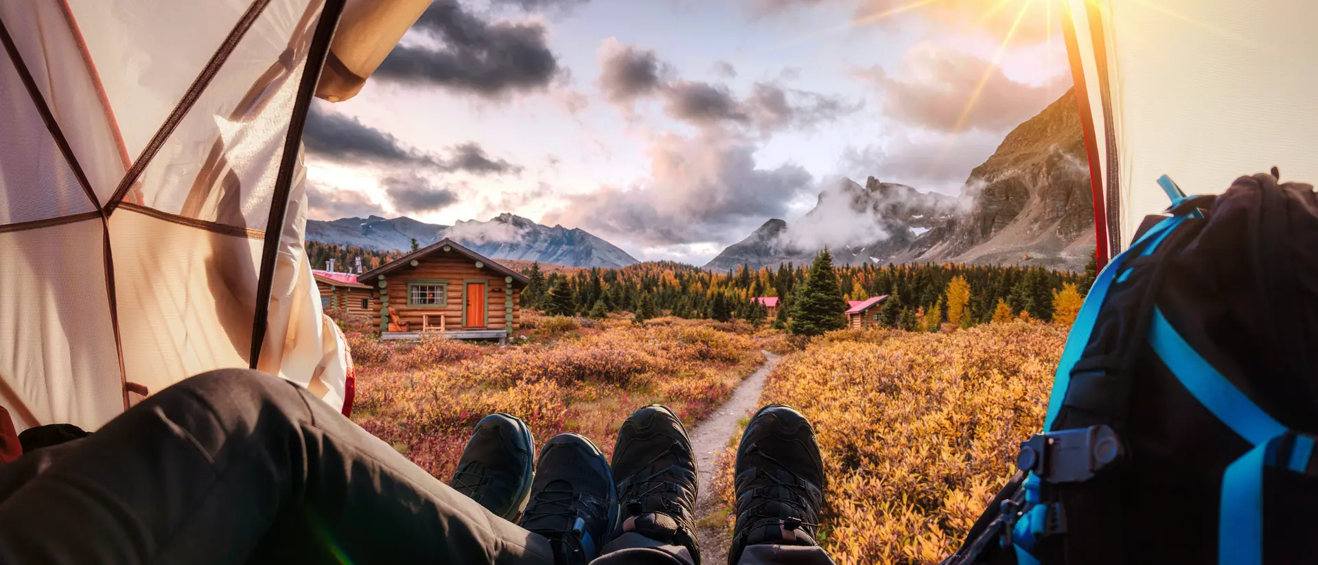 View from inside a tent, showing feet and backpacks, with mountains and a sunset in the background.