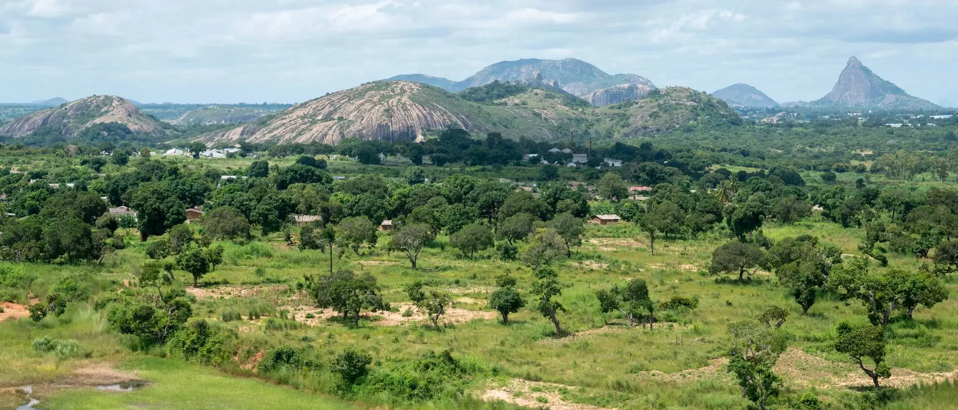 Lush green landscape with rolling hills and mountains under a partly cloudy sky.