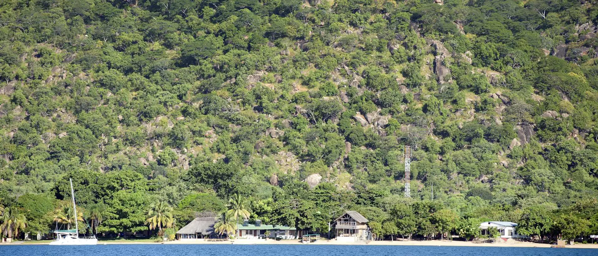 A panoramic view of Lake Malawi, Africa. The lake is surrounded by lush green hills and has crystal-clear blue water.