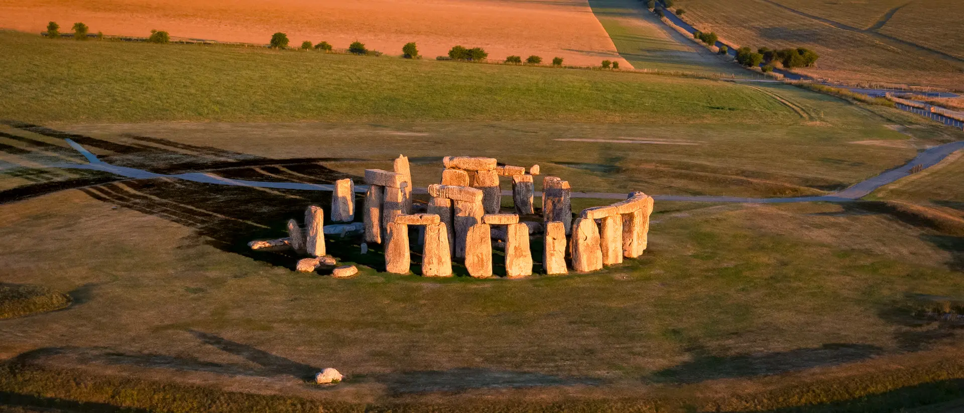 Aerial view of Stonehenge with surrounding fields under a clear blue sky during sunset.