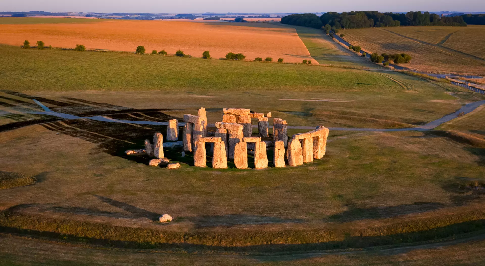 Aerial view of Stonehenge with surrounding fields under a clear blue sky during sunset.
