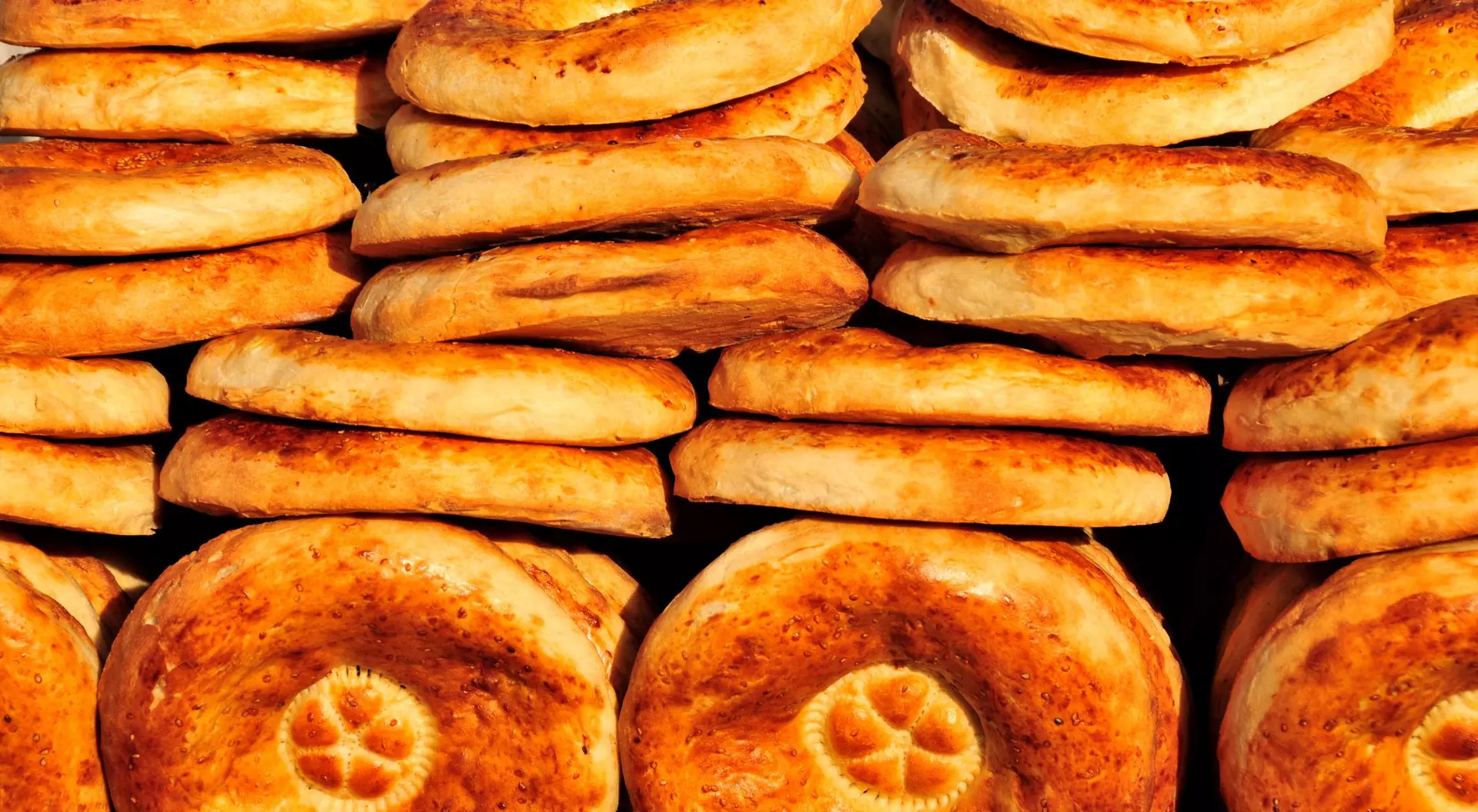 A stack of freshly baked round bread, golden brown with a slightly crisp surface and a decorative pattern on top.